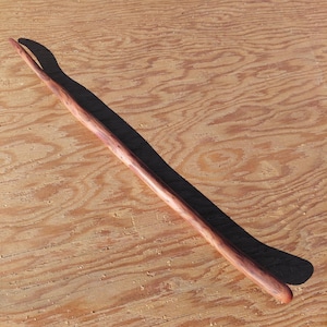 May include: A handcrafted wooden wand with a forked tip. The wand is a reddish-brown color and appears to be made from a single piece of wood. It is lying on a light brown wooden surface.