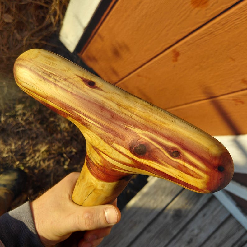 K&ouml;nnte beinhalten: Ein handgefertigter Holzspazierstock mit gebogenem Griff. Der Stock weist ein nat&uuml;rliches Holzmaserungsmuster mit Gelb-, Rot- und Braunt&ouml;nen auf. Der Griff ist glatt und abgerundet und f&uuml;r einen bequemen Griff und Halt konzipiert.