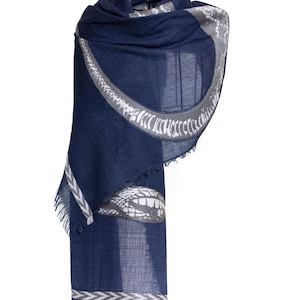 Peut inclure: Une écharpe bleu marine avec un motif de serpent gris et blanc. L'écharpe a un bord effiloché et une bordure décorative. Le motif de serpent est répété sur l'écharpe. L'écharpe est en matière souple.