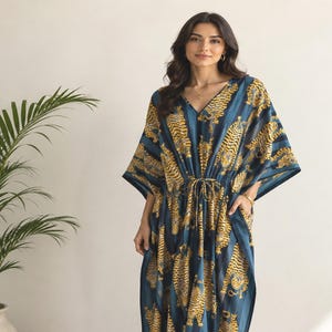 May include: A floor-length kaftan dress featuring a dark blue and teal vertical striped pattern with a repeating yellow and black tiger print. The garment has a V-neckline, wide kimono-style sleeves, and a drawstring waist tie for an adjustable fit.