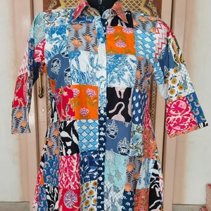 Puede incluir: Una camisa patchwork con botones y cuello. La camisa presenta una variedad de cuadrados estampados coloridos, incluyendo estampados florales, geométricos y de animales. Las mangas son de tres cuartos y la camisa se muestra en un maniquí.