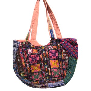 May include: A colorful, patchwork tote bag with a rounded shape. The bag features a variety of embroidered patterns in pink, yellow, blue, and green. The handles are a solid peach color.