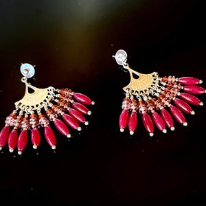 May include: A pair of dangle earrings with a gold fan-shaped design and red and pink beads.