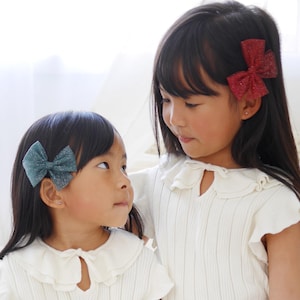 May include: Two young girls wearing white ruffled tops and tulle skirts. The girl on the left has a teal bow in her hair and the girl on the right has a red bow in her hair.