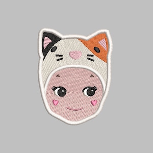 Op de afbeelding: Gestikt patch van een meisje dat een kattenkostuum draagt. Het kostuum is wit met oranje en zwarte accenten. Het meisje heeft roze wangen en een glimlach.