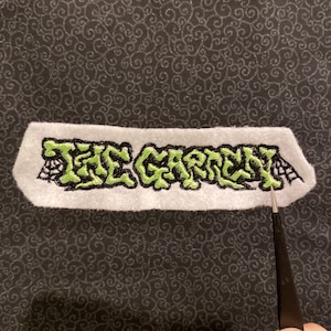 May include: Green embroidered patch with the text "THE CARNY" in a stylized font. The patch is on a white background and has a black outline.