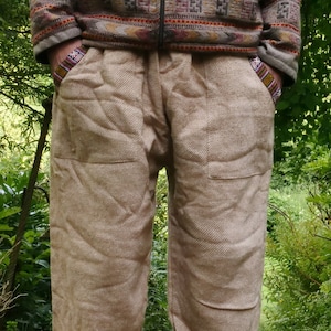 May include: Beige linen pants with a drawstring waist and cuffed legs. The pants have two large pockets on the front and a textured fabric.
