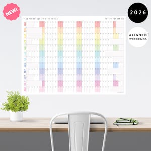 May include: A large wall calendar for 2026 with a rainbow colour scheme. The calendar is labelled "Plan the Things // Do the Things" and "Twenty Twenty Six." It features aligned weekends and is marked "NEW!"