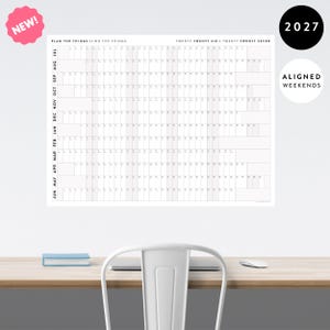 May include: A large white wall calendar featuring a grid layout for the years 2026 and 2027. The calendar displays months from July to June, with columns for days and aligned weekends. Text includes PLAN THE THINGS // DO THE THINGS and 2027.