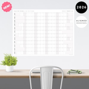 Peut inclure: Un grand calendrier mural blanc pour l'année 2026 avec le texte "PLAN THE THINGS // DO THE THINGS" et "TWENTY TWENTY SIX". Le calendrier a des week-ends alignés et un autocollant "NEW!".