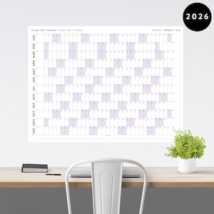 May include: A large white wall calendar for the year 2026, with a grid layout and purple-tinted boxes for each day. The text "PLAN THE THINGS // DO THE THINGS" is at the top. A black circle with "2026" is in the upper right corner.