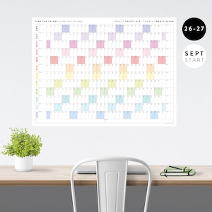 Peut inclure: Un grand calendrier mural intitulé PLAN THE THINGS // DO THE THINGS pour vingt vingt-six et vingt vingt-sept. La grille présente des lignes pour les mois de septembre à août avec des blocs de couleur pour les jours et les dates.