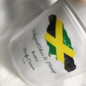 May include: A white plastic jar with a green, yellow and black Jamaican flag design. The jar is labelled "Whipped Shea & Mango butter Body Cream".