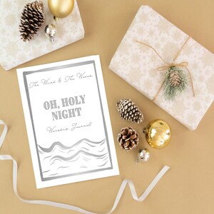 May include: A white printable journal with a silver border and the text "The Wind & The Waves" and "Oh, Holy Night Worship Journal". The journal is on a brown surface with pine cones, ornaments, and ribbon.