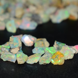 Könnte beinhalten: Eine Sammlung von rohen, natürlichen Opal-Edelsteinen. Die Opale sind in verschiedenen Schattierungen von Weiß, Grün und Blau mit irisierenden Farbschimmern.