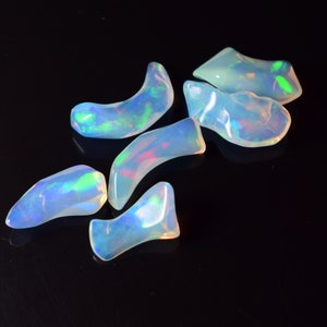 May include: A selection of iridescent opal gemstones, each with a unique, organic shape. The opals display a play of colour, with flashes of blue, green, and pink hues. The gemstones are set against a dark background.
