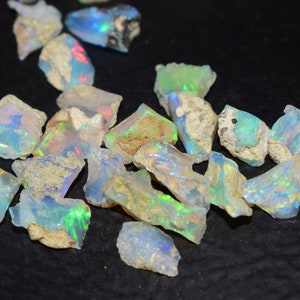 Könnte beinhalten: Eine Sammlung von rohen, natürlichen Opal-Edelsteinen. Die Opale sind eine Mischung aus weißen, blauen, grünen und irisierenden Farben. Die Steine sind unregelmäßig geformt und haben eine raue, natürliche Textur.