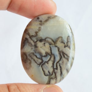 May include: A round, white agate cabochon with brown and gray dendritic patterns. The stone is smooth and polished.