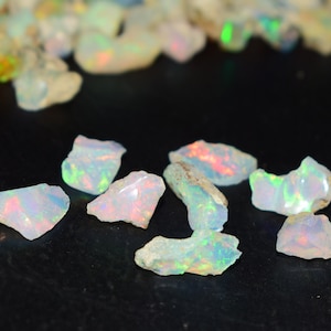Könnte beinhalten: Eine Sammlung von weißen Opal-Edelsteinen mit schillernden Regenbogenfarben. Die Opale sind roh und haben eine natürliche, unregelmäßige Form.