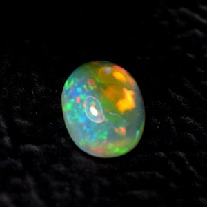 Könnte beinhalten: Ein runder, irisierender Opal-Edelstein mit einem weißen, grünen, orangefarbenen und roten Farbmuster. Der Opal ist vor einem schwarzen Hintergrund platziert.