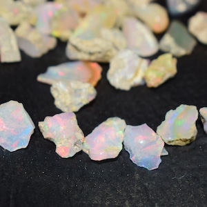 Könnte beinhalten: Eine Sammlung von rohen, weißen Opal-Edelsteinen mit schillernden Regenbogenfarben. Die Opale sind in verschiedenen Größen und Formen.
