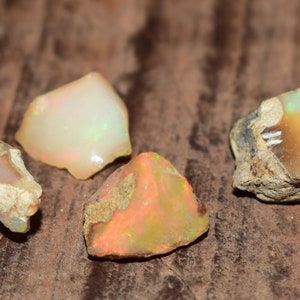 May include: Four rough opal stones with a variety of colours and textures. The stones are on a brown background.