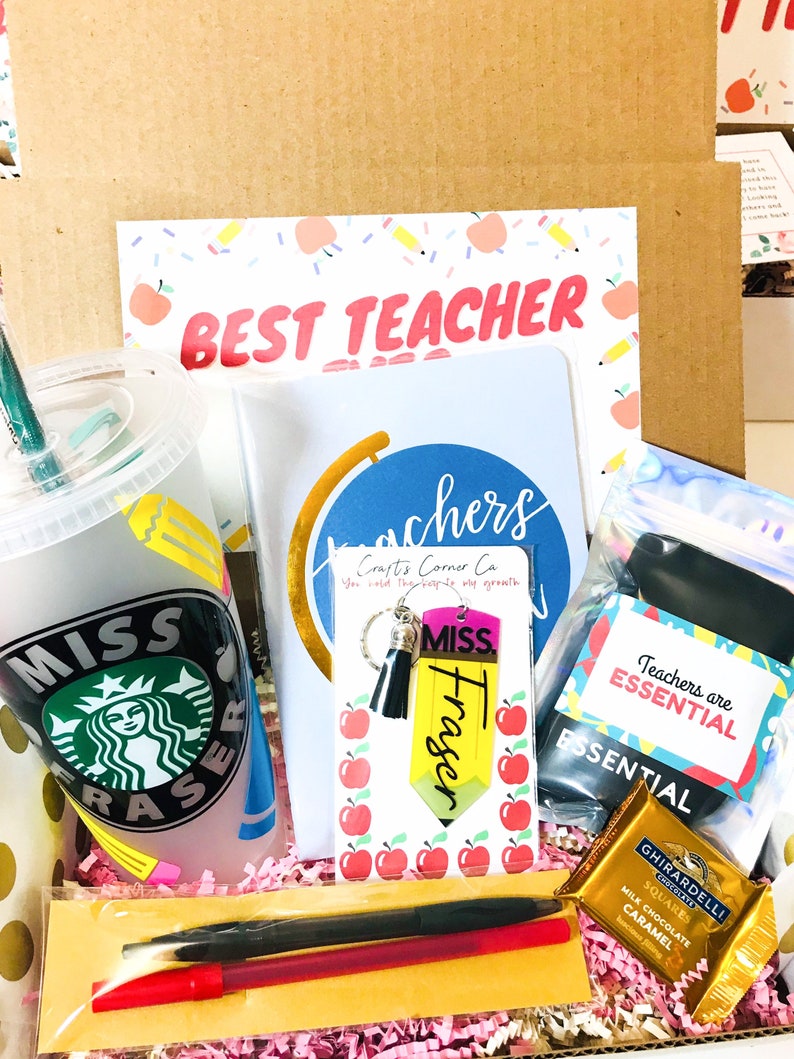 May include: A gift box filled with teacher appreciation gifts, including a reusable cup with a green logo, a notebook with the words "Teachers you hold the hope of growth", a keychain with a pencil charm, a chocolate bar, and a red pen.