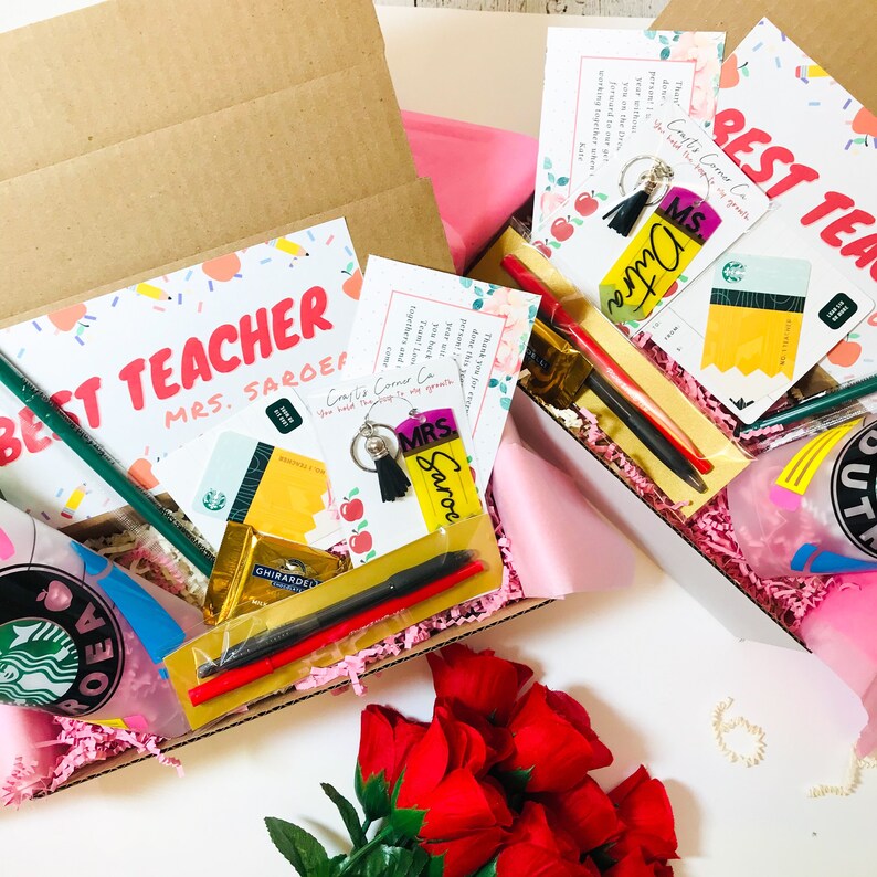 May include: Two gift boxes filled with teacher appreciation gifts. The boxes are lined with pink tissue paper and contain items such as gift cards, pens, a keychain, and a coffee cup. The boxes are labeled "Best Teacher" and "Best Teacher Mrs. Saroe".