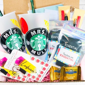 May include: A gift box filled with teacher appreciation gifts, including two personalized Starbucks cups, a keychain, socks, chocolate, and a note that says "Teachers are essential".