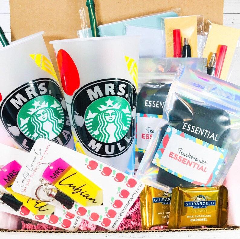 May include: A gift box filled with teacher appreciation gifts, including two personalized Starbucks cups, a keychain, socks, chocolate, and a note that says "Teachers are essential".