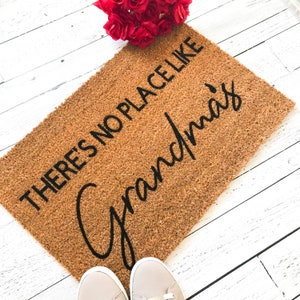 Puede incluir: Una alfombra de coco marr&oacute;n con el texto "There's no place like Grandma's" en letras negras.