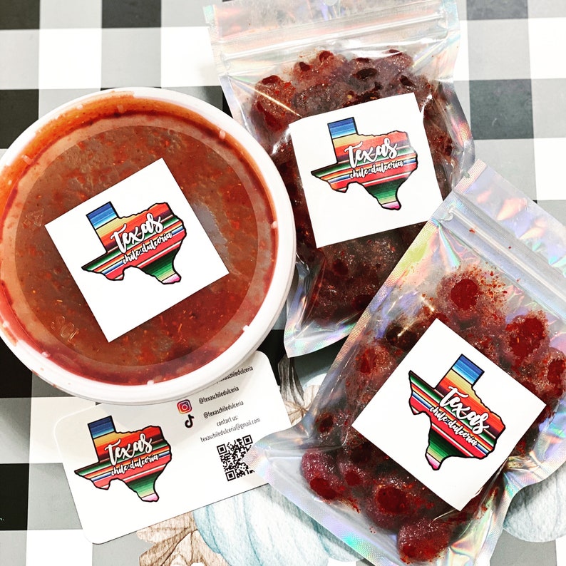 May include: A white container of red sauce and two clear bags of red candies. Each item has a sticker with a Texas outline and the words "Texas chile dulceria". The background is a black and white checkered pattern.