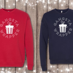 Puede incluir: Dos sudaderas, una roja y otra azul marino, con un gráfico blanco de una caja de regalo y el texto "Gangsta Wrapper" en un círculo.