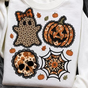 May include: A white sweatshirt featuring a graphic print of a leopard-print ghost with an orange plaid bow, a floral pumpkin, a floral skull, and a spider web. The designs are outlined with black lace trim and surrounded by small orange pumpkins and leaves.