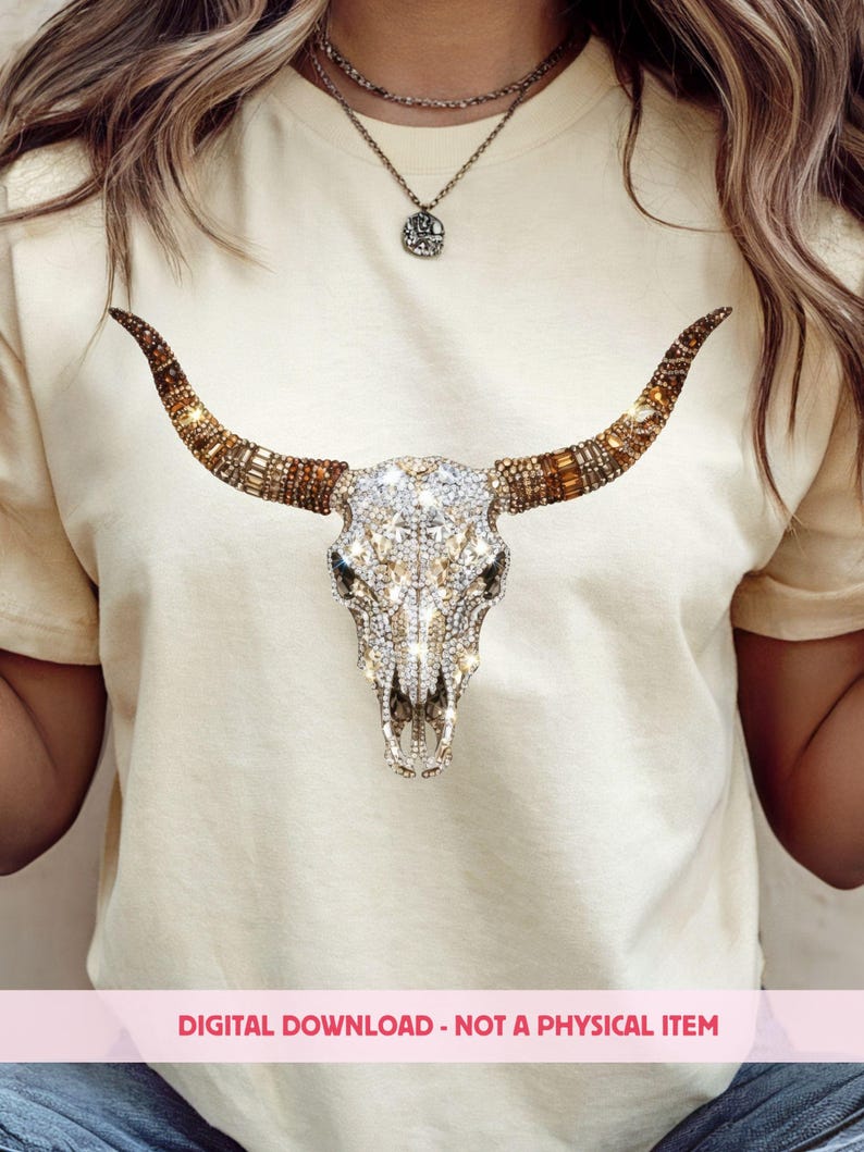 May include: A cream-colored t-shirt featuring a central graphic of a bull skull adorned with sparkling clear and amber-toned rhinestones. The skull design includes long, curved horns decorated with brown and gold crystals. Text reads: DIGITAL DOWNLOAD - NOT A PHYSICAL ITEM.