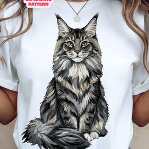 Puede incluir: Camiseta blanca con una ilustración detallada de un gato Maine Coon. El gato está representado en tonos grises y marrones, con ojos amarillos y una cola esponjosa. El texto en la camiseta dice "NOT A CUTTING OR SEWING PATTERN" y "DIGITAL DOWNLOAD - NOT A PHYSICAL ITEM."