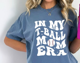 May include: A blue t-shirt with the text "In My T-Ball Mom Era" in white with a baseball graphic.