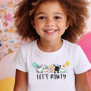 May include: A white t-shirt with a graphic of five dogs wearing party hats and holding balloons. The text "Let's Pawty" is printed below the dogs.