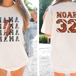May include: Two white t-shirts with a football theme. One shirt says "MAMA" with a lightning bolt and football graphic. The other shirt says "NOAH 32" with a football graphic.