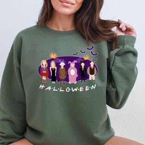 May include: A green sweatshirt featuring a graphic print of the characters from the TV show "Friends" dressed in Halloween costumes. The text "HALLOWEEN" is printed below the characters.