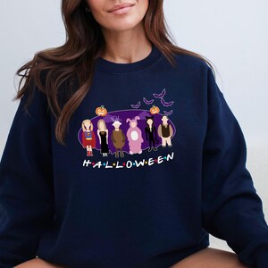 May include: A navy blue sweatshirt featuring a graphic of six cartoon characters dressed in Halloween costumes. The characters are standing in front of a purple background with bats and a pumpkin. The text "HALLOWEEN" is printed below the characters.