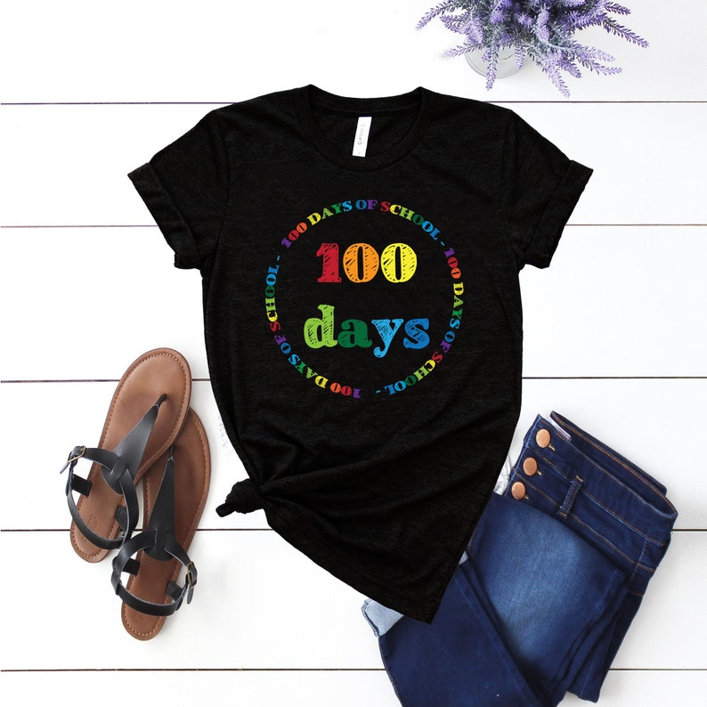 Puede incluir: Una camiseta negra de manga corta con un estampado gr&aacute;fico colorido. El dise&ntilde;o incluye el texto 100 days en letras grandes y multicolores, rodeado por un borde circular con el texto repetido 100 DAYS OF SCHOOL en colores del arco&iacute;ris.