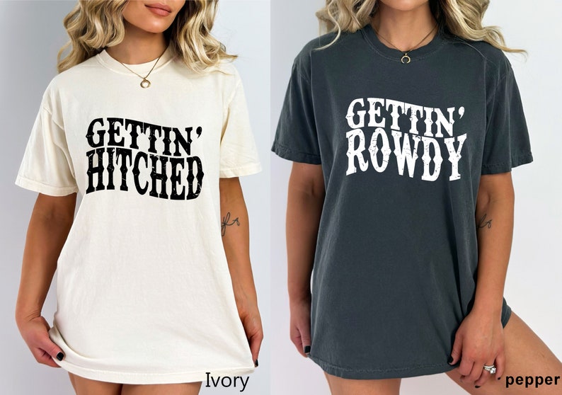 May include: Two women wearing oversized t-shirts. The shirt on the left is ivory with black text that says "Gettin' Hitched". The shirt on the right is dark gray with white text that says "Gettin' Rowdy".