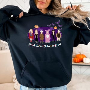 May include: Black hooded sweatshirt featuring a graphic print of the characters from the TV show "Friends" dressed in Halloween costumes. The text "HALLOWEEN" is printed below the characters.