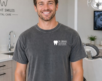 May include: A gray t-shirt with the text "DR. BRIAN BASTROP FAMILY DENTISTRY" and a tooth graphic. The person in the image is smiling. The background includes dental equipment and a dental office setting.