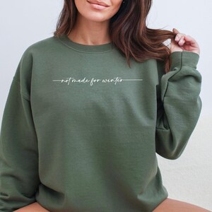 May include: A green sweatshirt with the text "not made for winter" in white lettering.