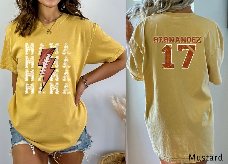 May include: A mustard yellow t-shirt with a football and lightning bolt graphic on the front and the text "MAMA" repeated four times. The back of the shirt has the text "HERNANDEZ" and the number "17" in a distressed style.