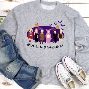 May include: A grey sweatshirt with a purple background featuring six cartoon characters dressed in Halloween costumes. The characters are standing in a line and the text "H.A.L.L.O.W.E.E.N" is below them. There are bats and a pumpkin above the characters.