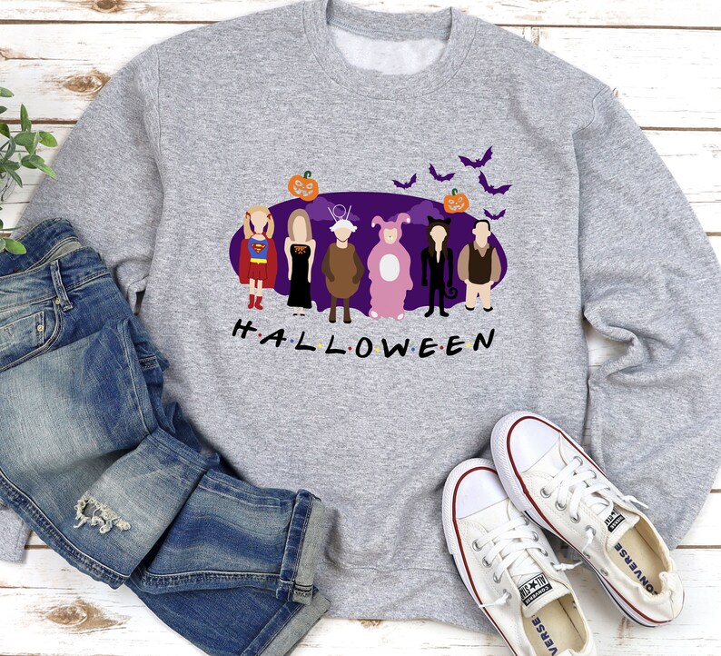 May include: A grey sweatshirt with a purple background featuring six cartoon characters dressed in Halloween costumes. The characters are standing in a line and the text "H.A.L.L.O.W.E.E.N" is below them. There are bats and a pumpkin above the characters.