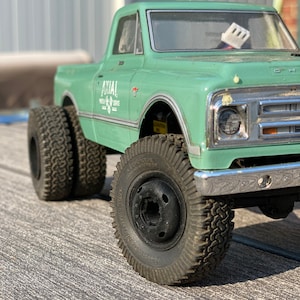 Könnte beinhalten: Ein grüner Spielzeug-LKW mit schwarzen Reifen und den Worten "AXIAL" und "WHEELS & SERVICE" an der Seite.